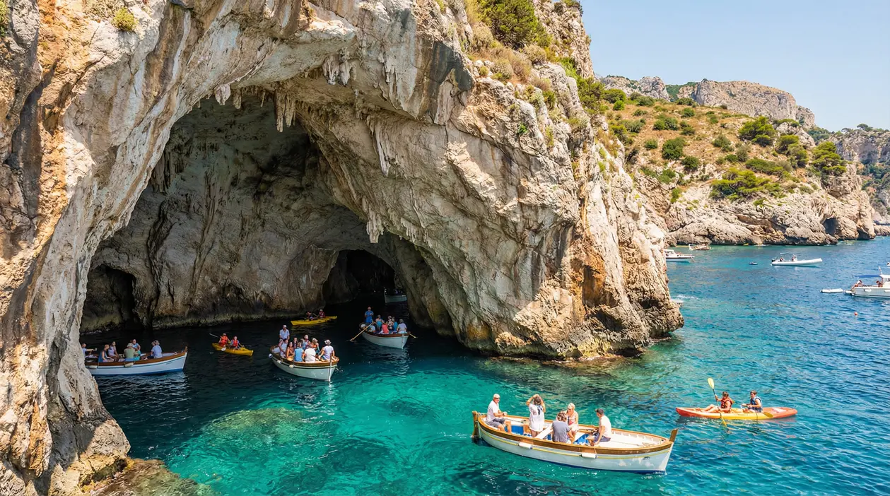 Ingresso di una grotta marina in una scogliera, con barche e kayak su acqua turchese
