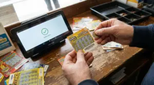 Mani che controllano un gratta e vinci con una moneta accanto a un terminale di verifica in tabaccheria